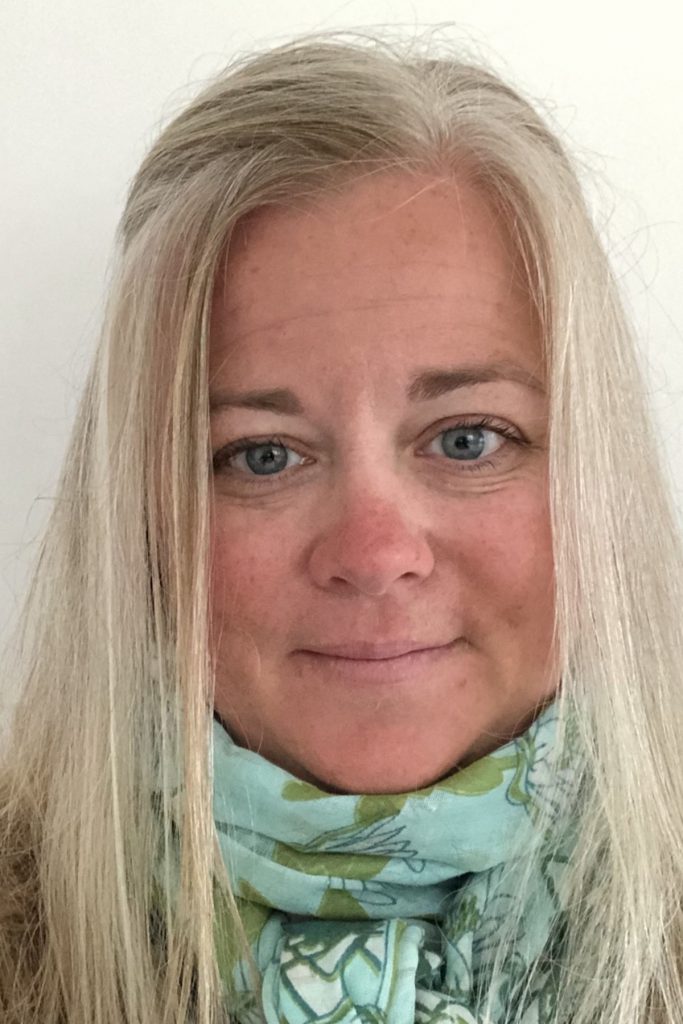 Portrait of Laurene M. McKenna, wearing a light-colored patterned scarf, smiling into the camera