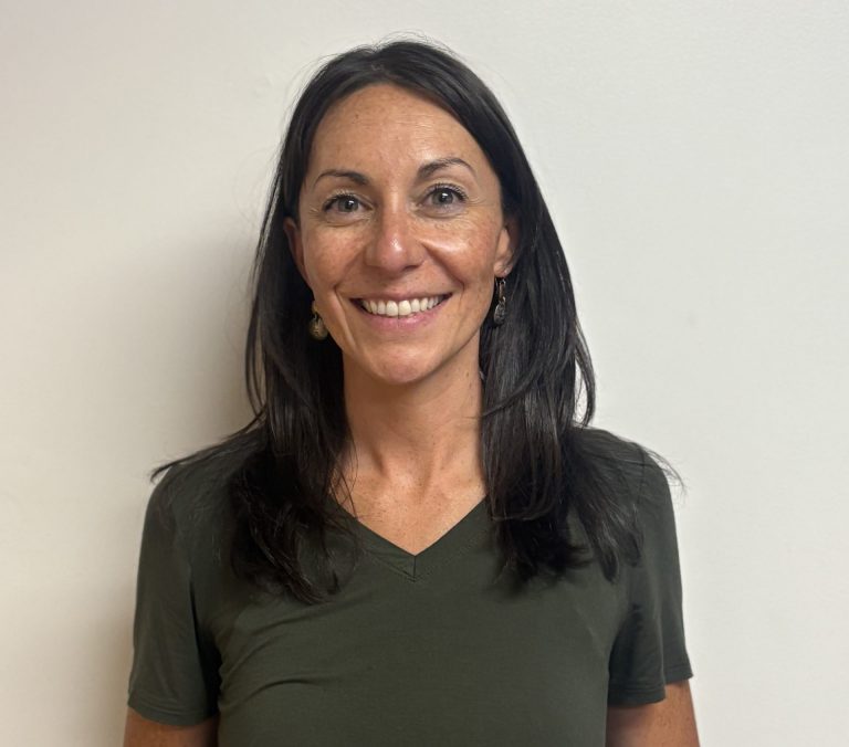 Headshot of aeowyn brust, a smiling woman with shoulder-length dark hair wearing an olive green v-neck top.