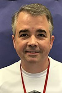 Headshot of robert england, a smiling man with short brown hair wearing a white shirt and red lanyard.