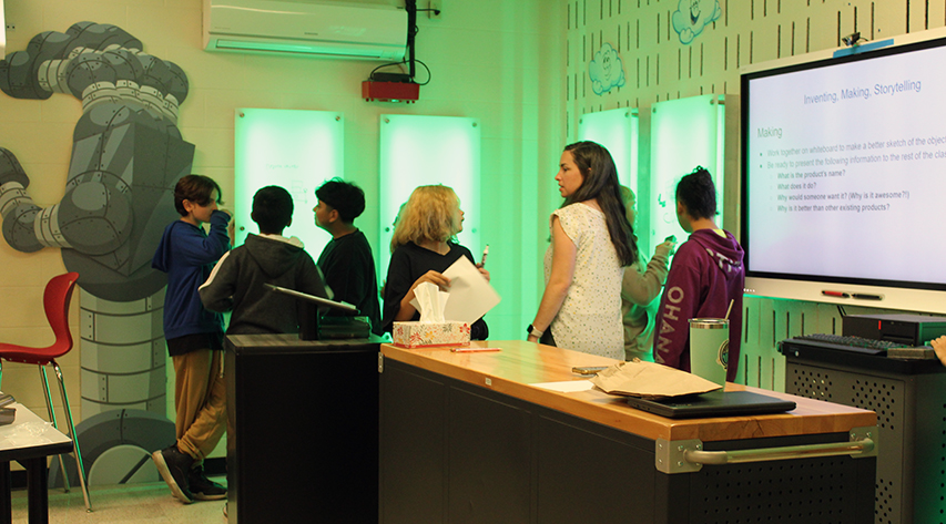classroom at liberty central school district, students and teacher gathered around teachers desk, projecter in ceiling projecting image onto screen
