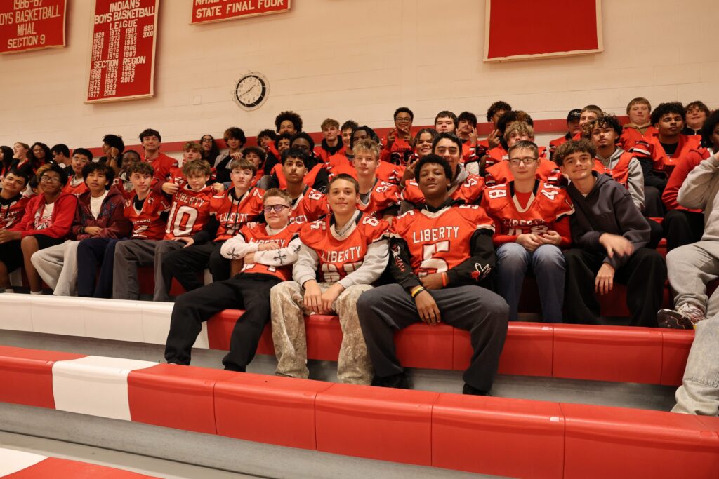 A group of Liberty football players and students sitting on bleachers in a gymnasium.