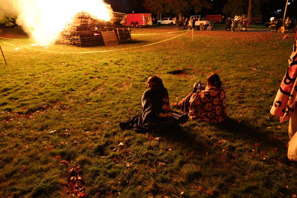 Spectators sitting on the field watching the evening bonfire during a Liberty Central School District event.