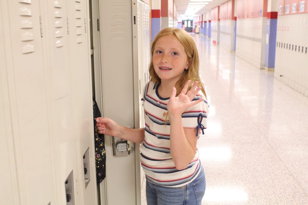 young elementary student smiling waving to camera while at locker