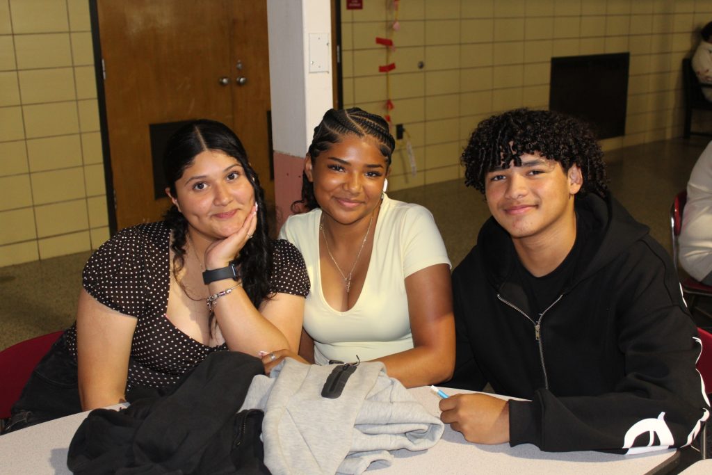 three students at a table in the cafeteria smiling