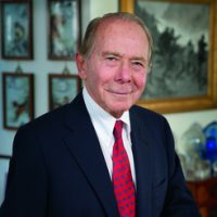 maurice greenburg, alumni of liberty and honoree of wall of fame, posing for photo, with suit and red tie, smiling, framed photos in background