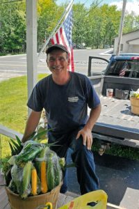 daniel thalmann, alumni of liberty and honoree of wall of fame, outside photo, posing for photo, with basket of veggies, truck and american flag behind them